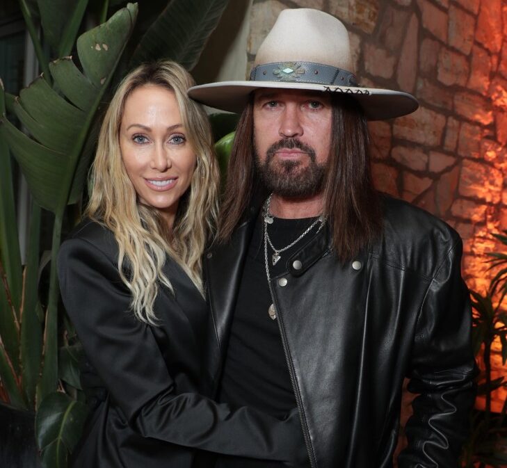 Tish Cyrus, in a black satin jacket, and Billy Ray Cyrus, in a black leather jacket and cowboy hat, pose for a photo.