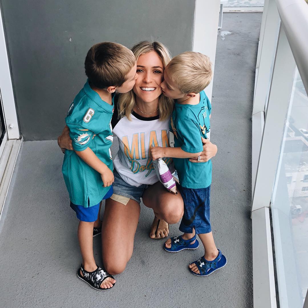 Kristin Cavallari kneeling between her two sons as they kiss her cheeks.