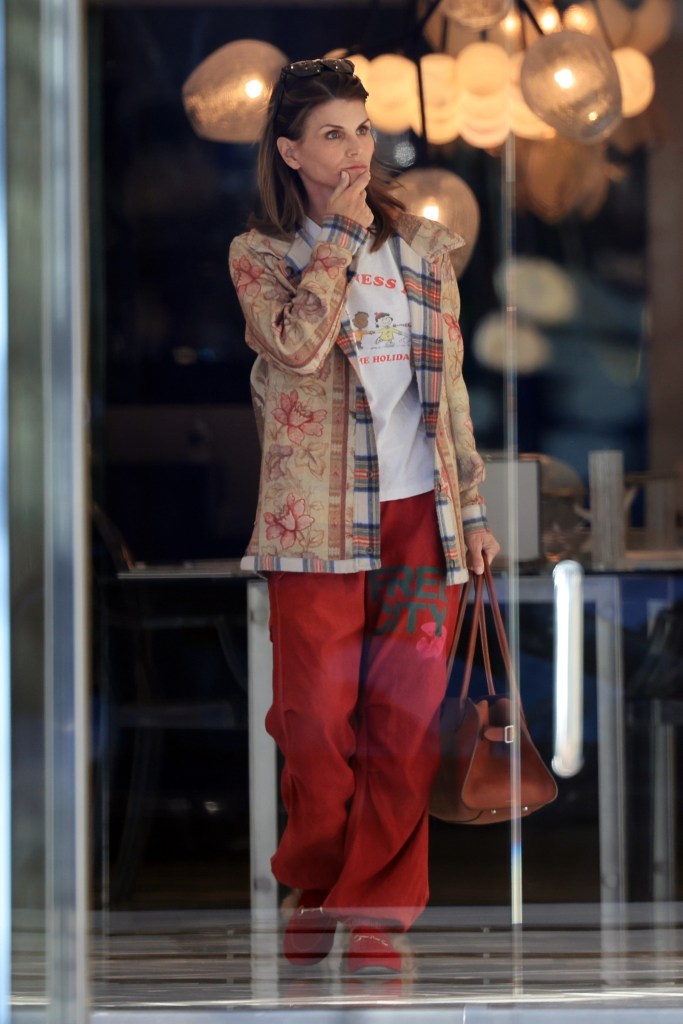 Lori Loughlin wearing a patterned jacket, plaid shirt, white T-shirt, and red pants while out shopping.