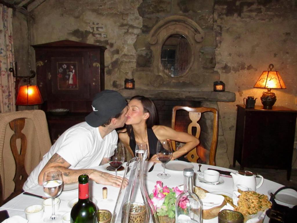 Brooklyn Beckham kissing Nicola Peltz at a dinner table.