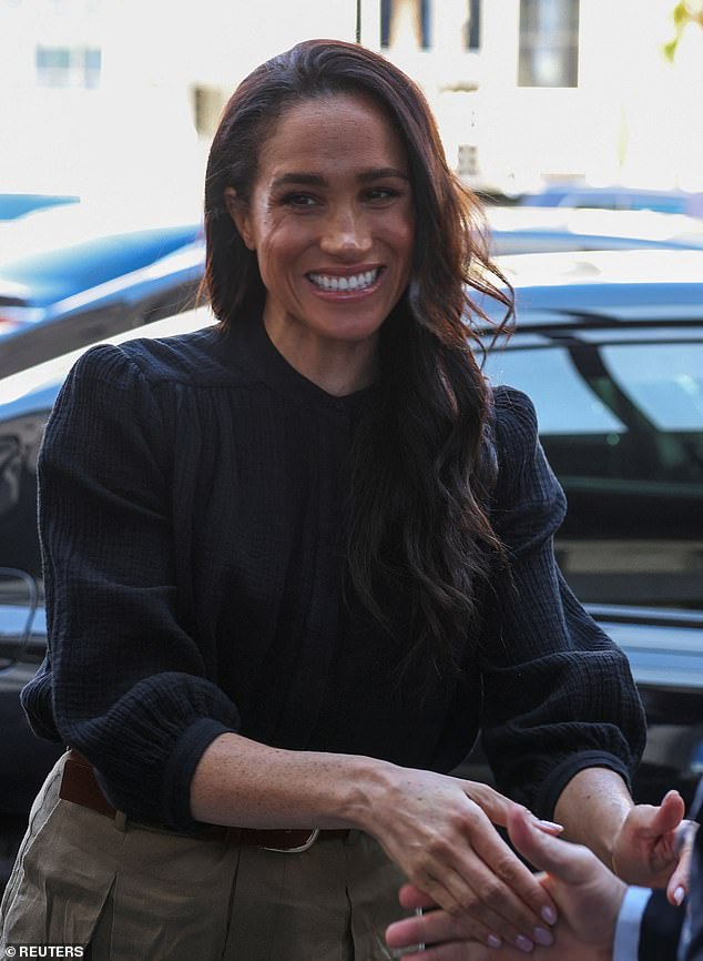 Meghan Markle later in the day wearing a black blouse, keeping the same creased trousers.