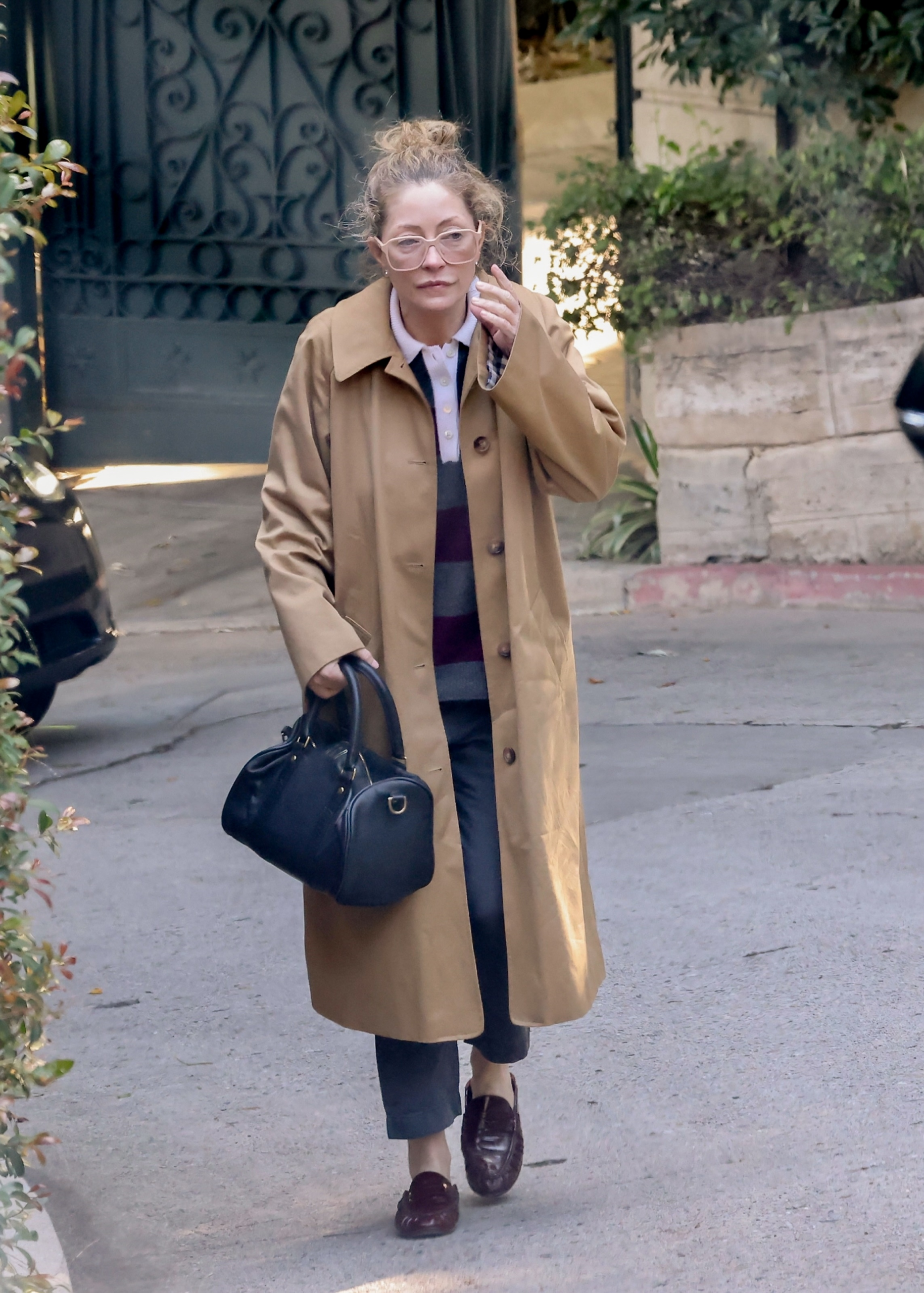 Rebecca Gayheart leaves the Los Angeles home days after Eric Dane's death, wearing a beige trench coat and glasses and carrying a black handbag.