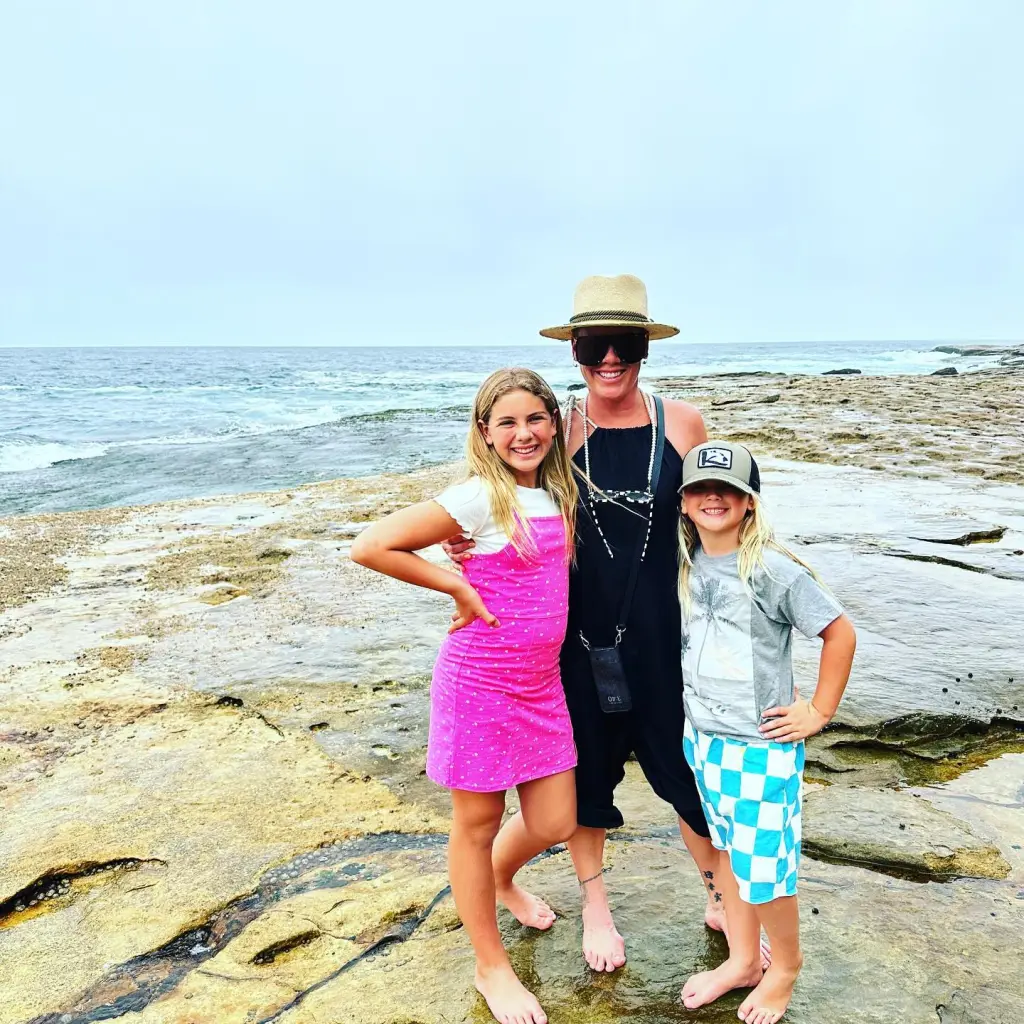 Pink, Carey Hart, and their kids standing on rocks by the ocean.