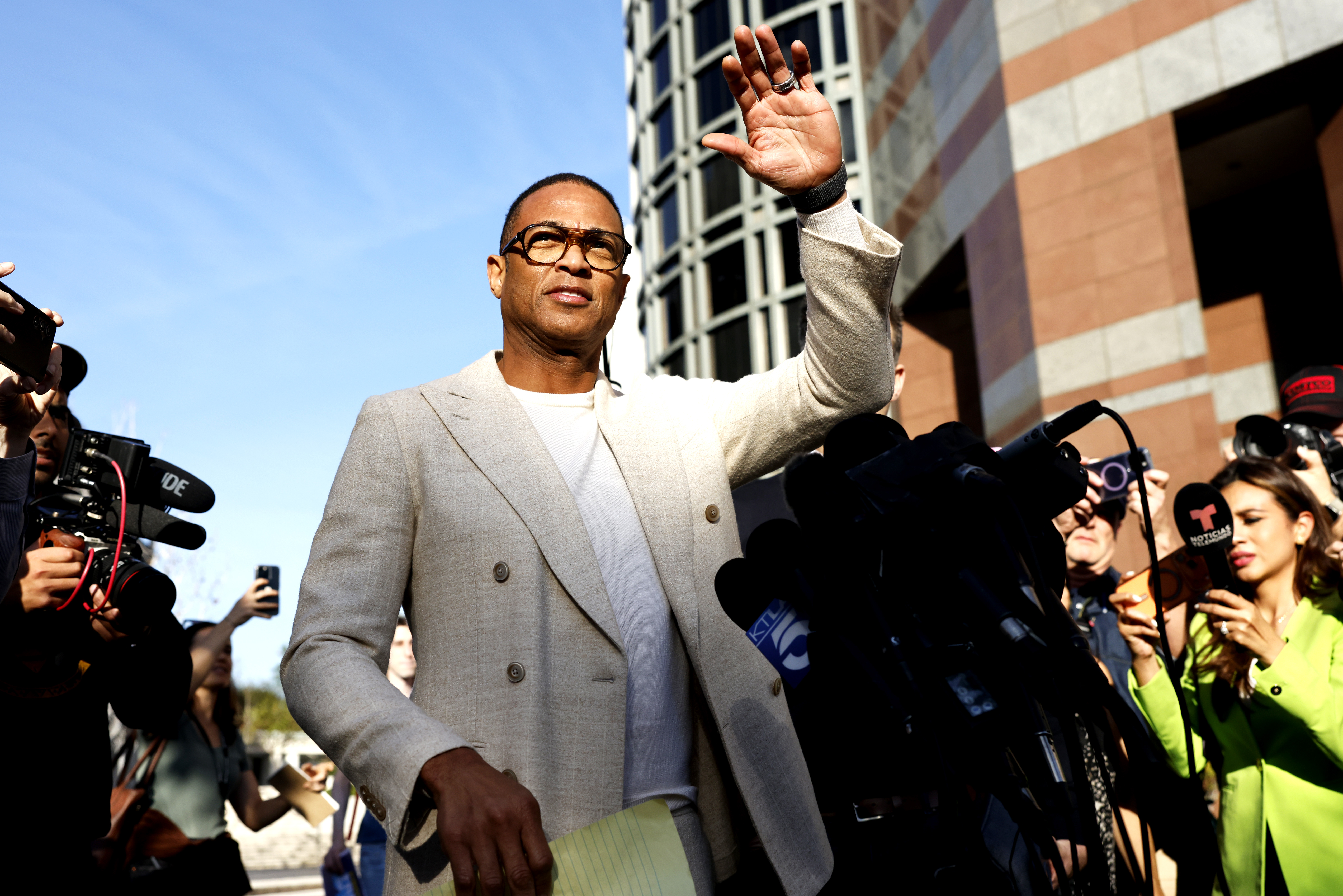 Journalist Don Lemon waves while surrounded by reporters and microphones outside a federal courthouse.