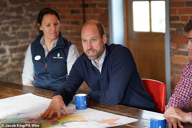Prince William seated at a table, looking at documents and a map