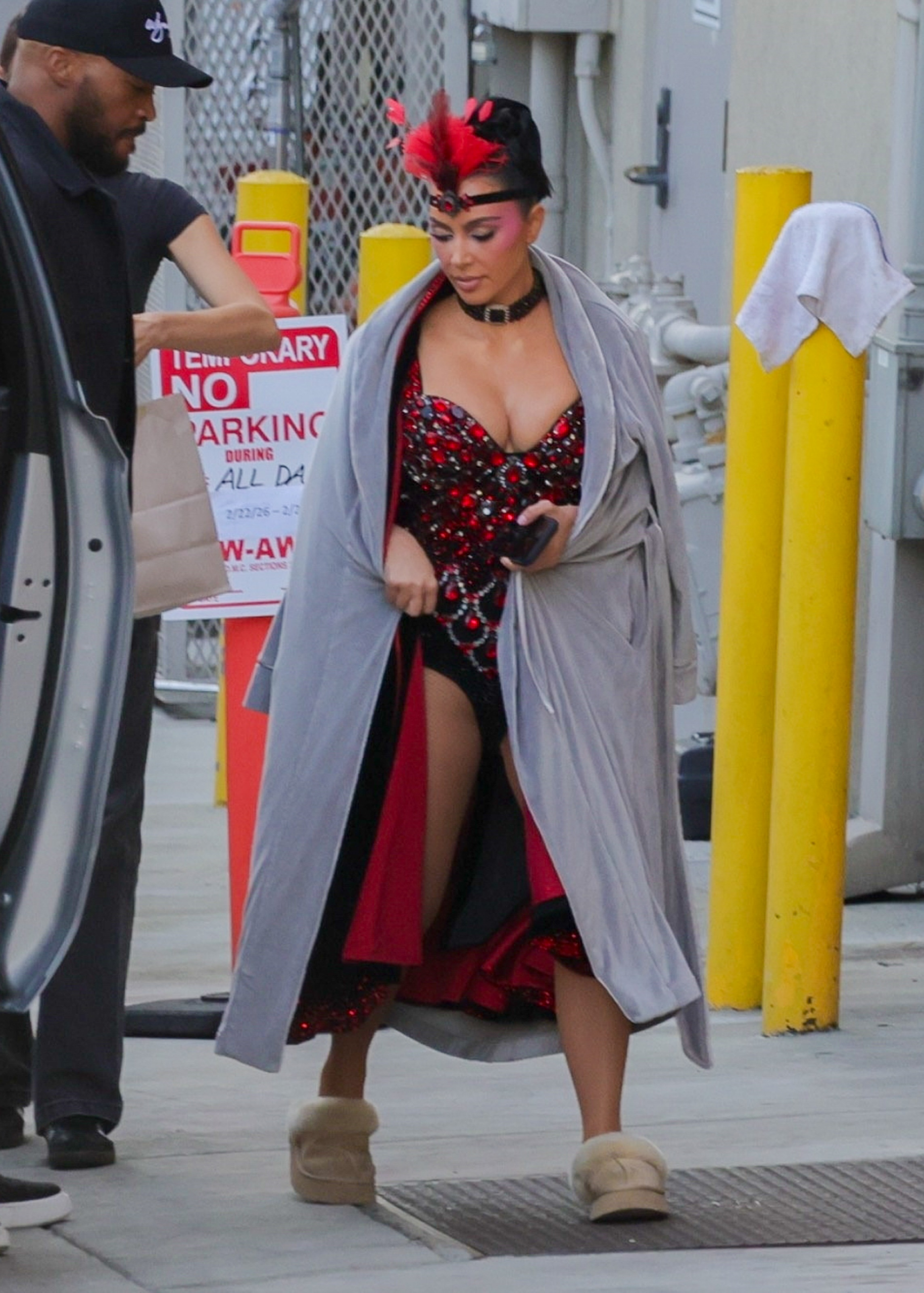 Kim Kardashian in a red and black showgirl costume, gray robe, and Ugg slippers on the set of The Fifth Wheel.