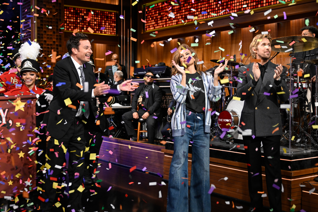 Jimmy Fallon, Eva Mendes, and Ryan Gosling clap as confetti falls on The Tonight Show set.