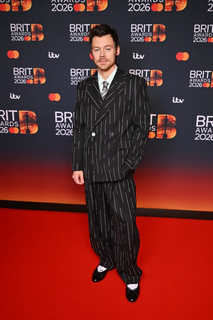 Harry Styles on the 2026 BRIT Awards red carpet wearing a black pinstriped Chanel suit.