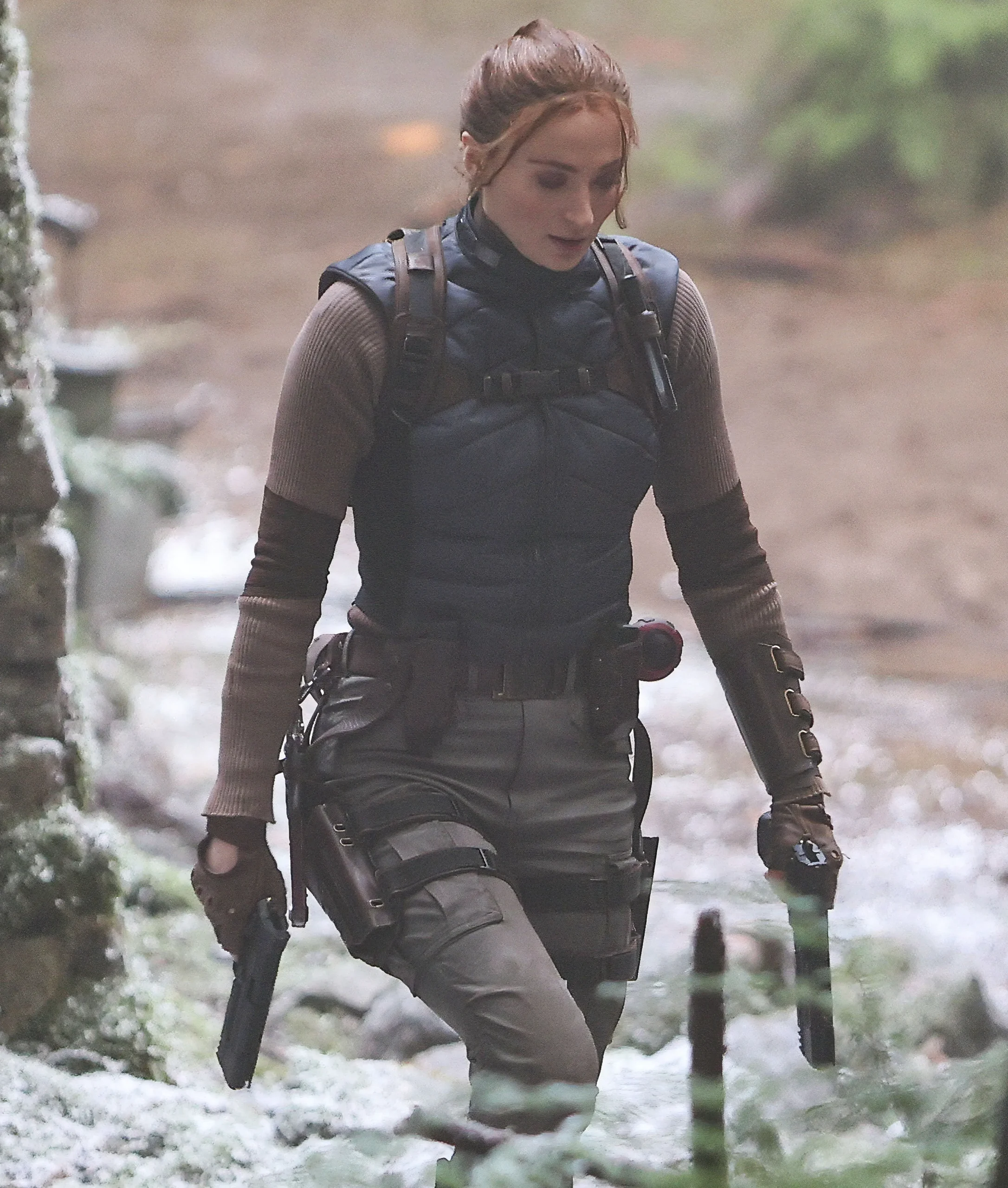 Sophie Turner in Lara Croft costume filming action scenes in a forest setting.