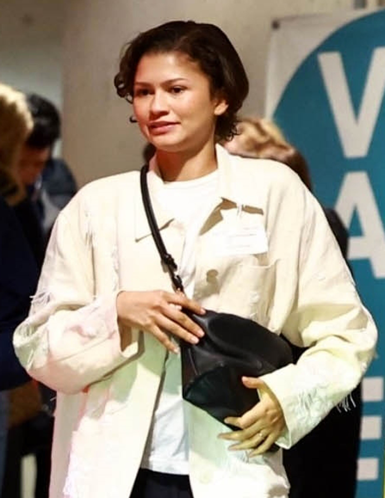 Zendaya in a white shirt and black pants, carrying a black designer bag and wearing a simple band on her left ring finger.