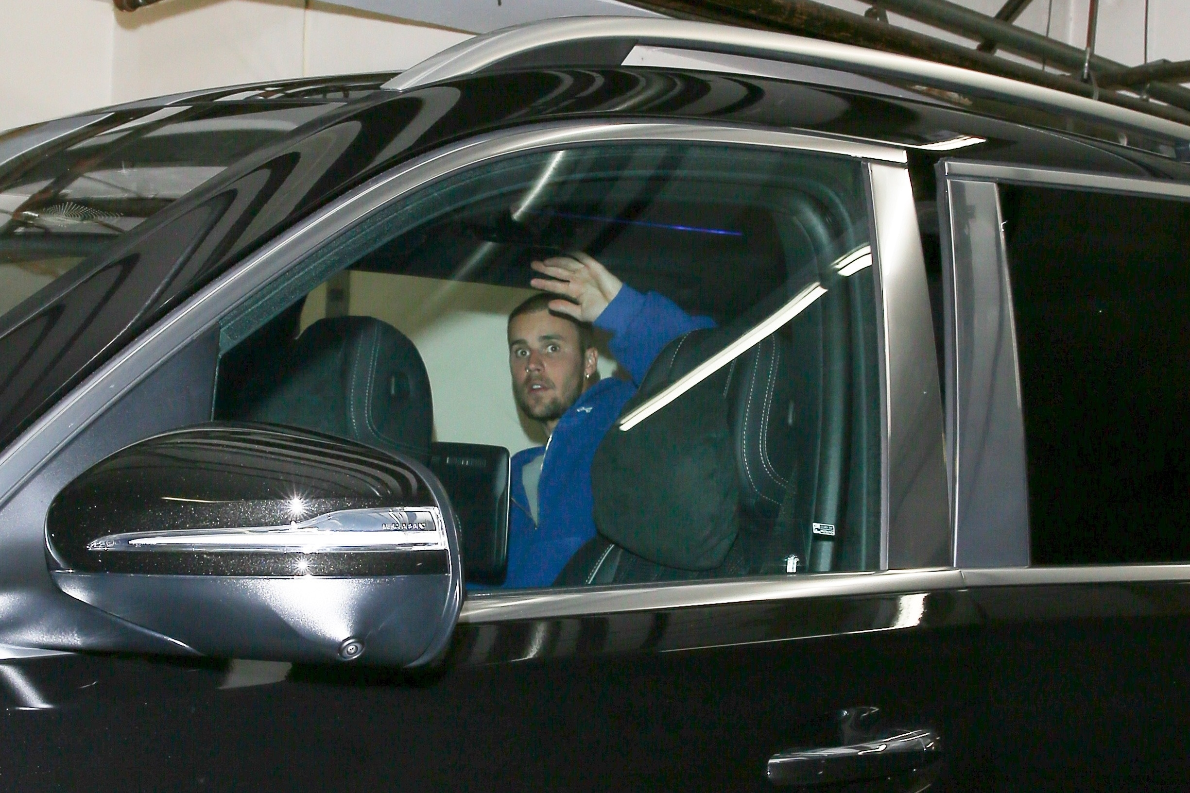 Justin Bieber raises a hand to block photographers while seated in a car.