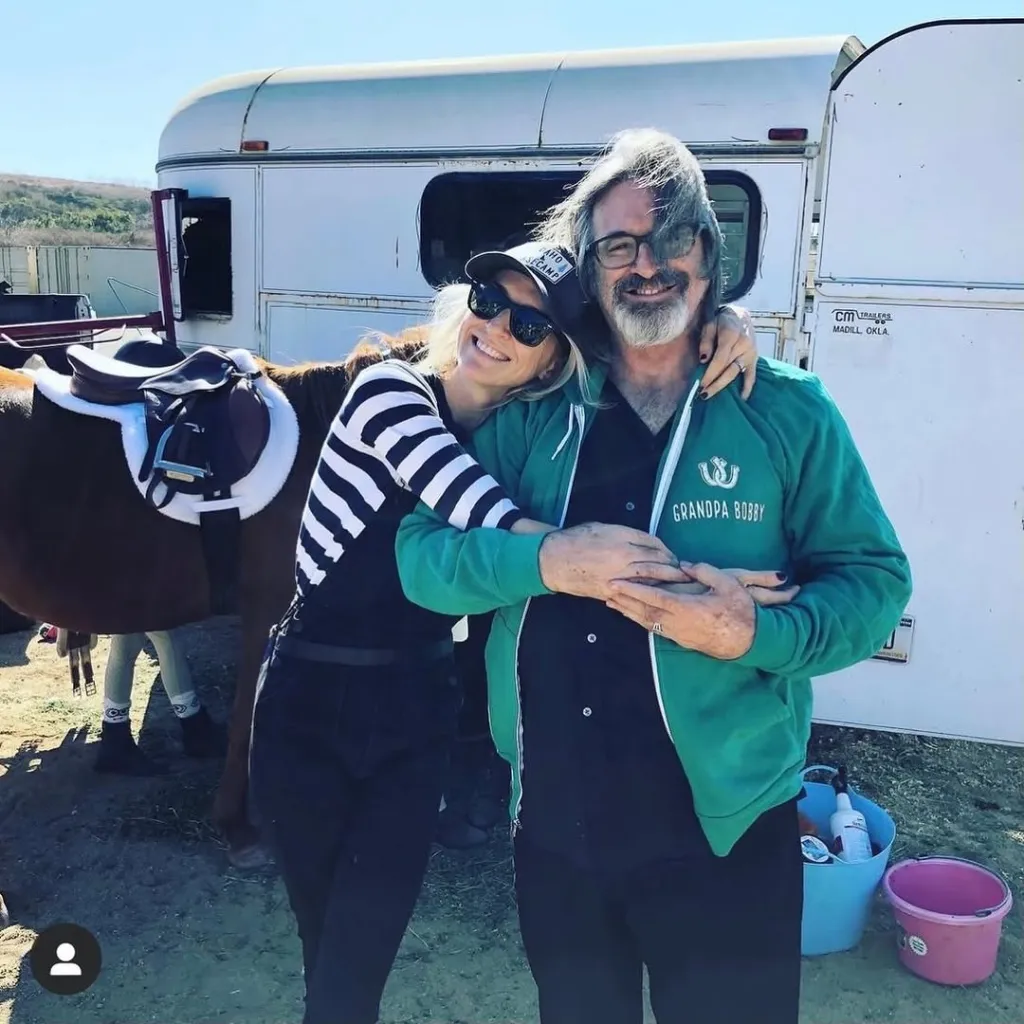 Robert Carradine and Ever Carradine embracing, standing next to a saddled horse and a trailer.