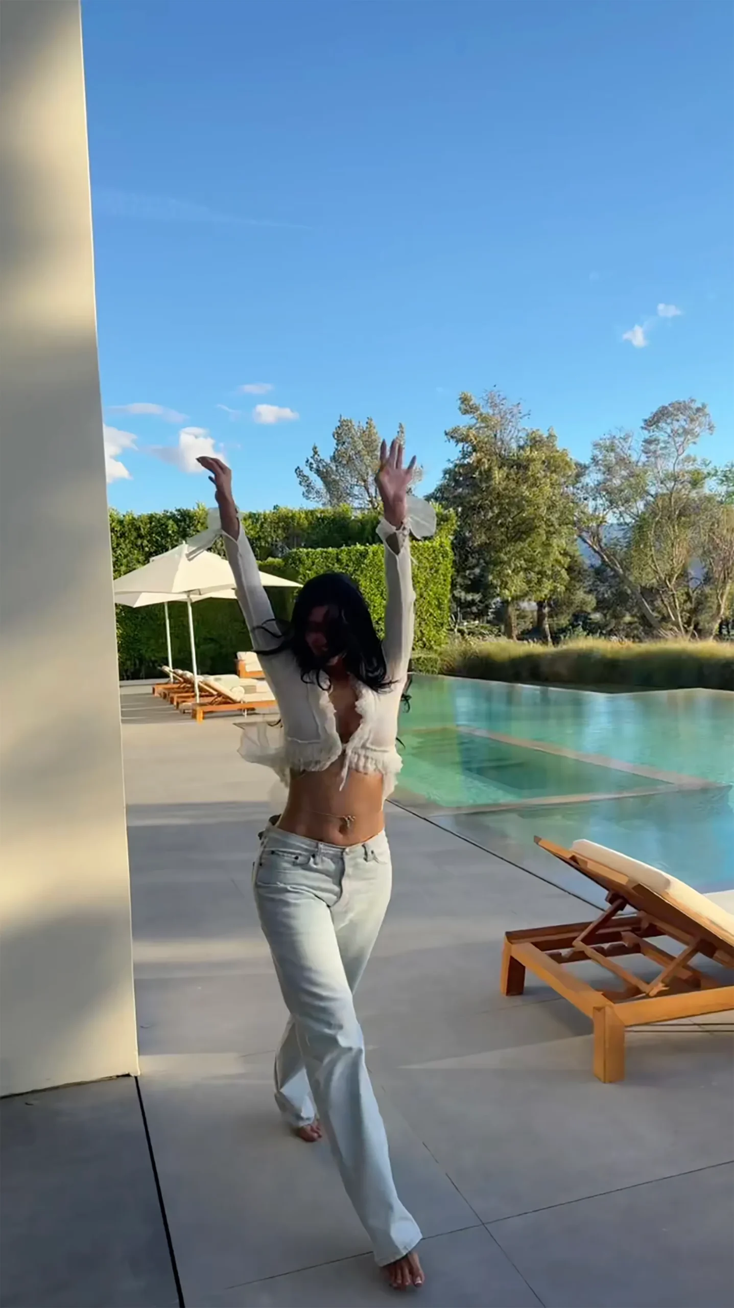 Kylie Jenner posing next to a pool with her arms raised.