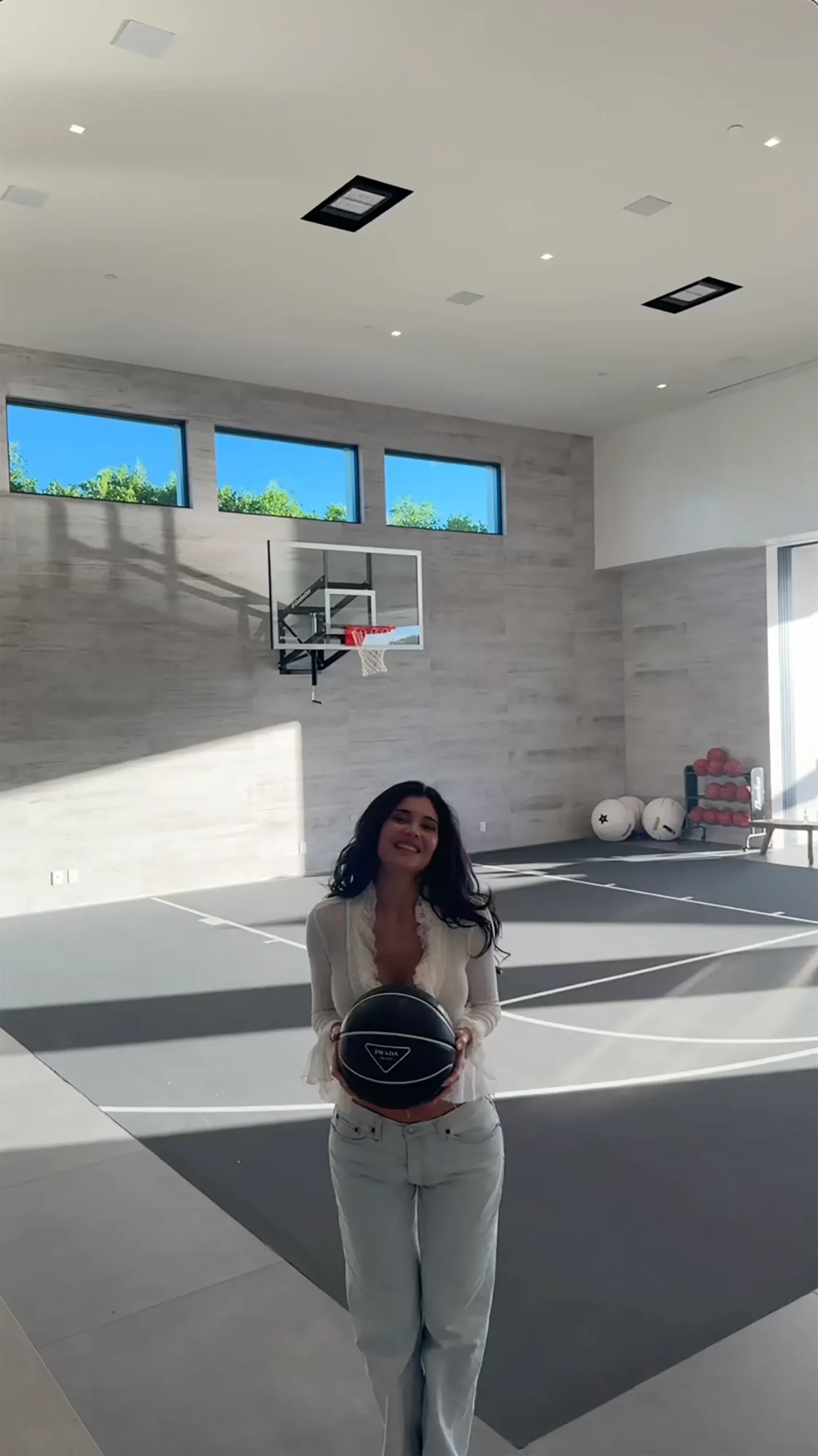 Kylie Jenner stands on an indoor basketball court, holding a black Prada basketball.