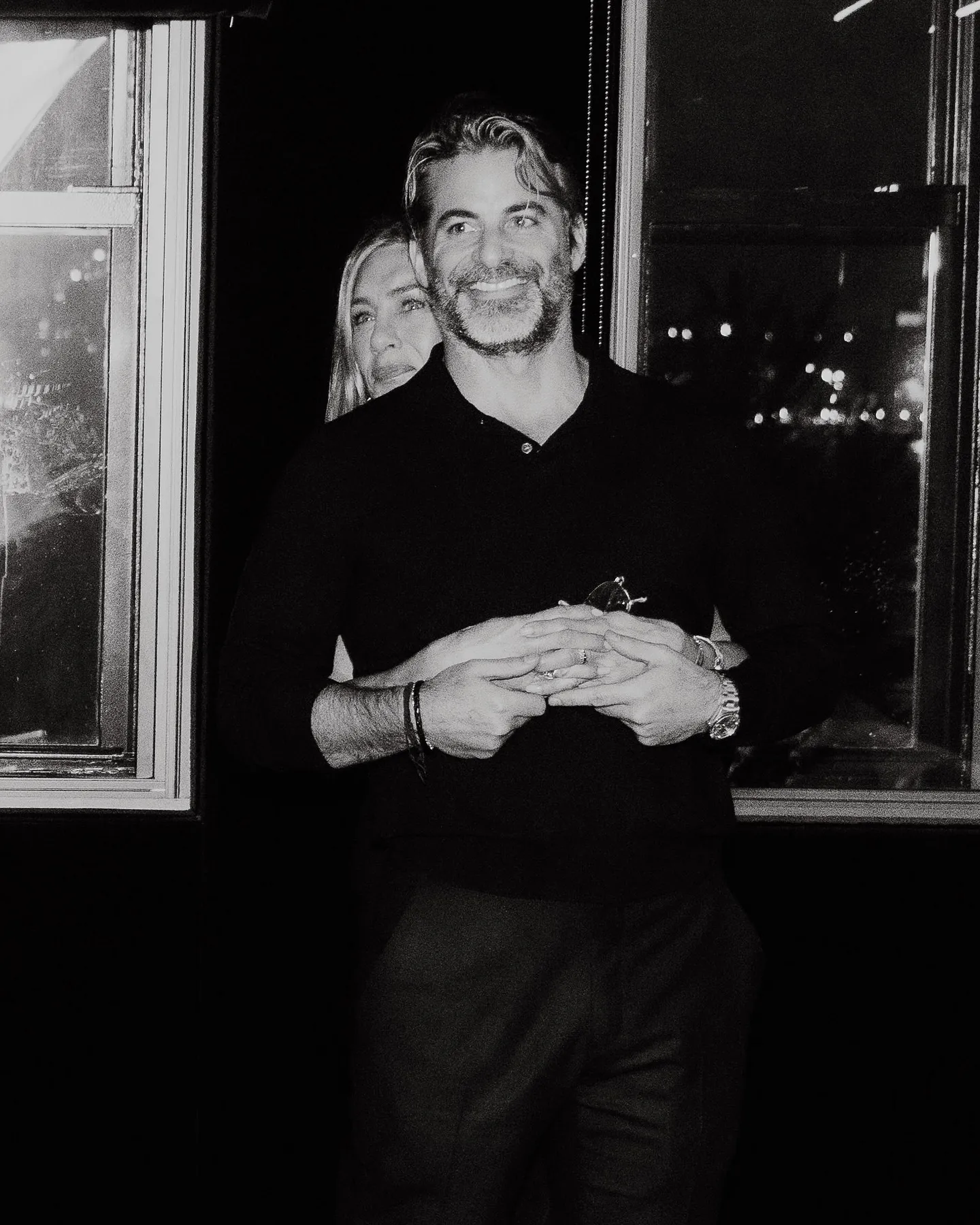 Jennifer Aniston embracing Jim Curtis from behind, smiling as they hold hands.