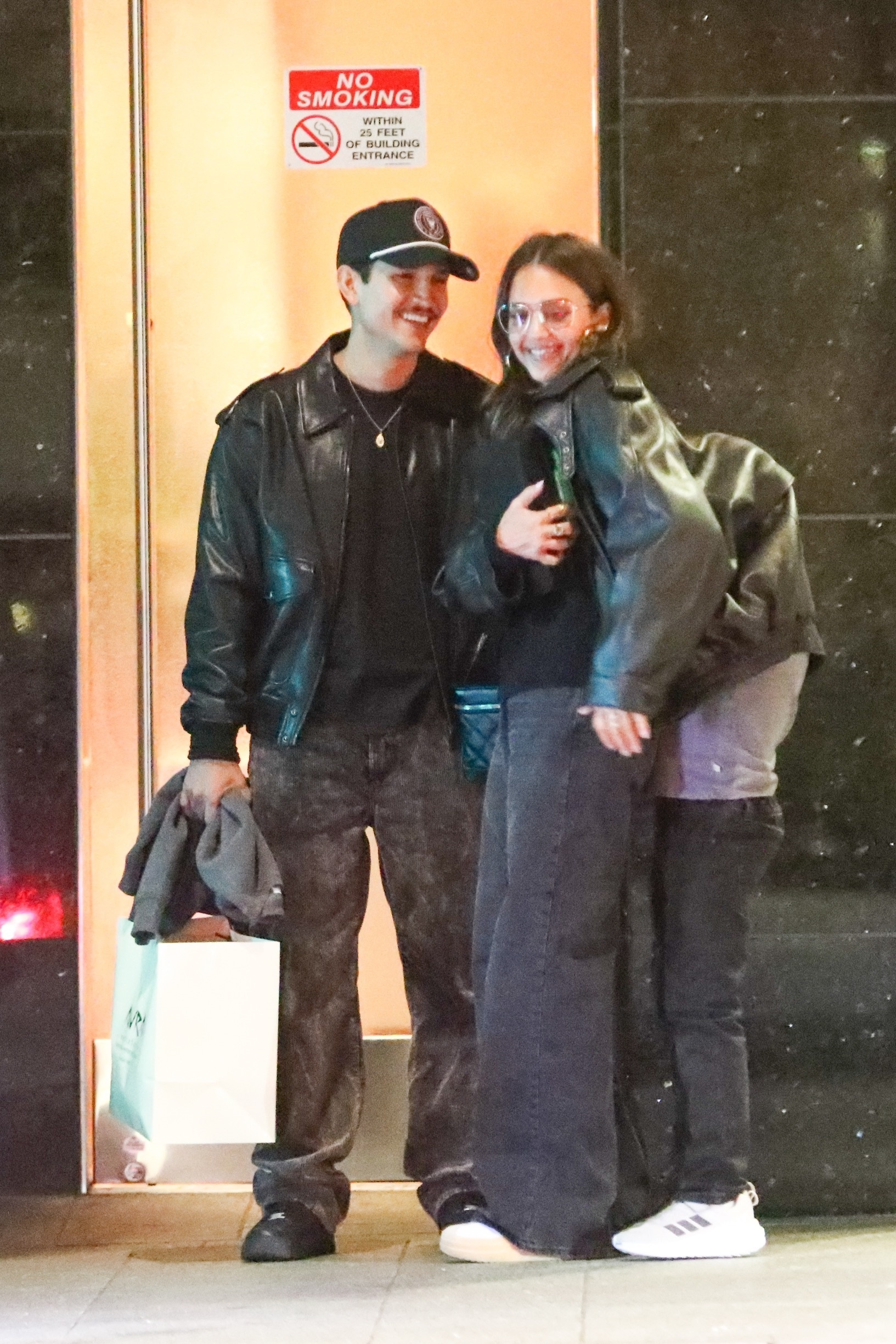 Jessica Alba smiles as her son Hayes tucks under her jacket while Danny Ramirez stands beside them outside Avra.