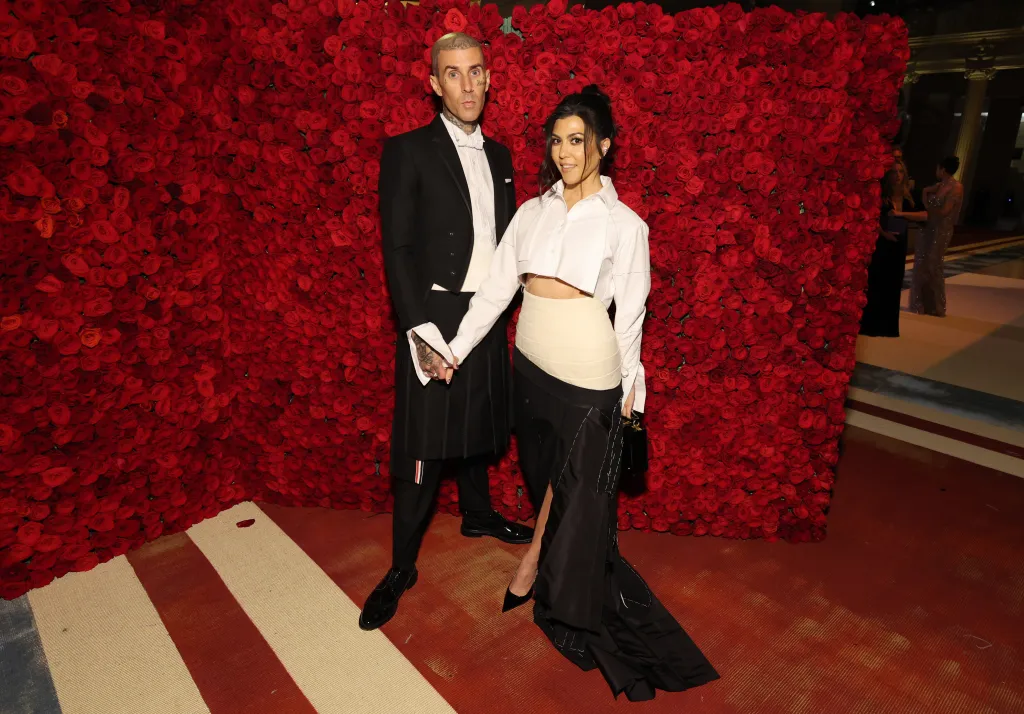 Kourtney Kardashian and Travis Barker at the Met Gala, posing together against a red rose backdrop.