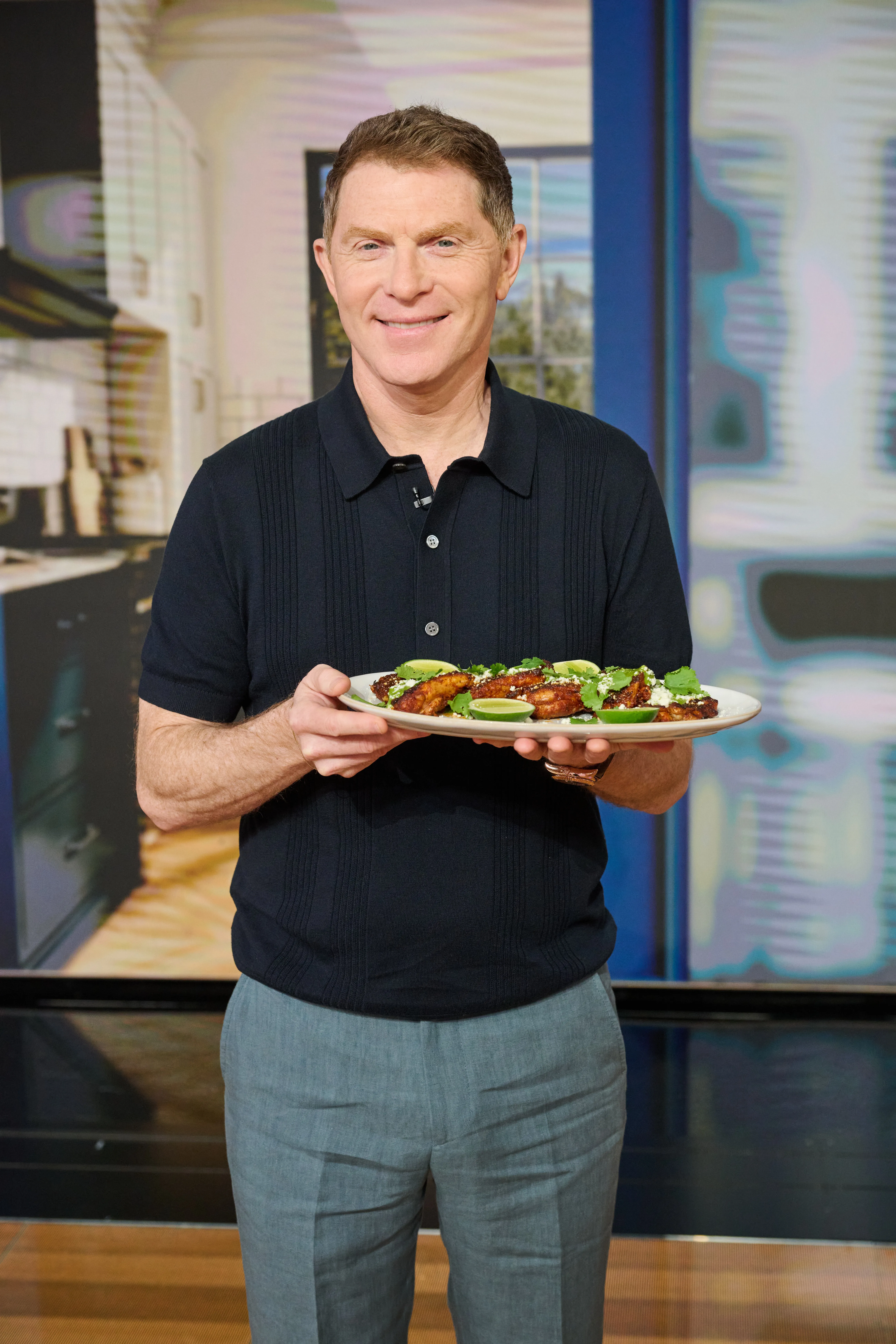 Celebrity chef Bobby Flay holds a plated dish and smiles at the camera.