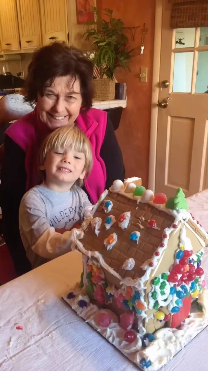 Nancy Guthrie and her grandson pose with a gingerbread house.