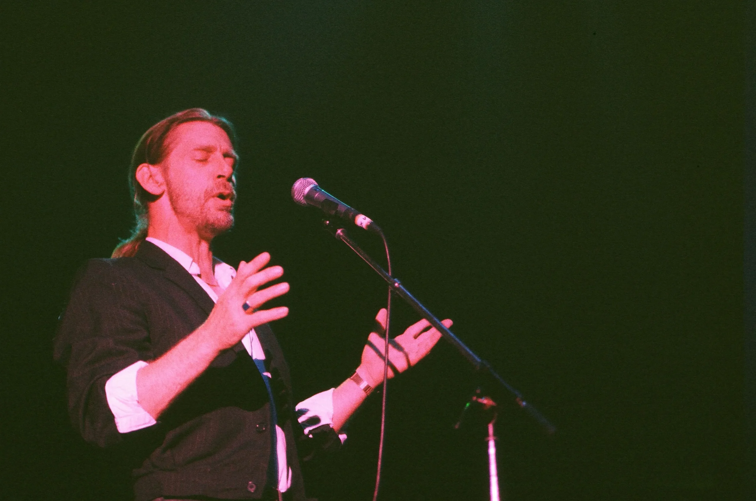 Alex Ligertwood singing into a microphone onstage.