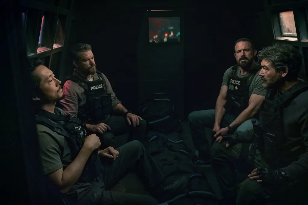 Steven Yeun, Matt Damon, Ben Affleck, and Kyle Chandler, all wearing tactical vests, sit inside a dark vehicle.
