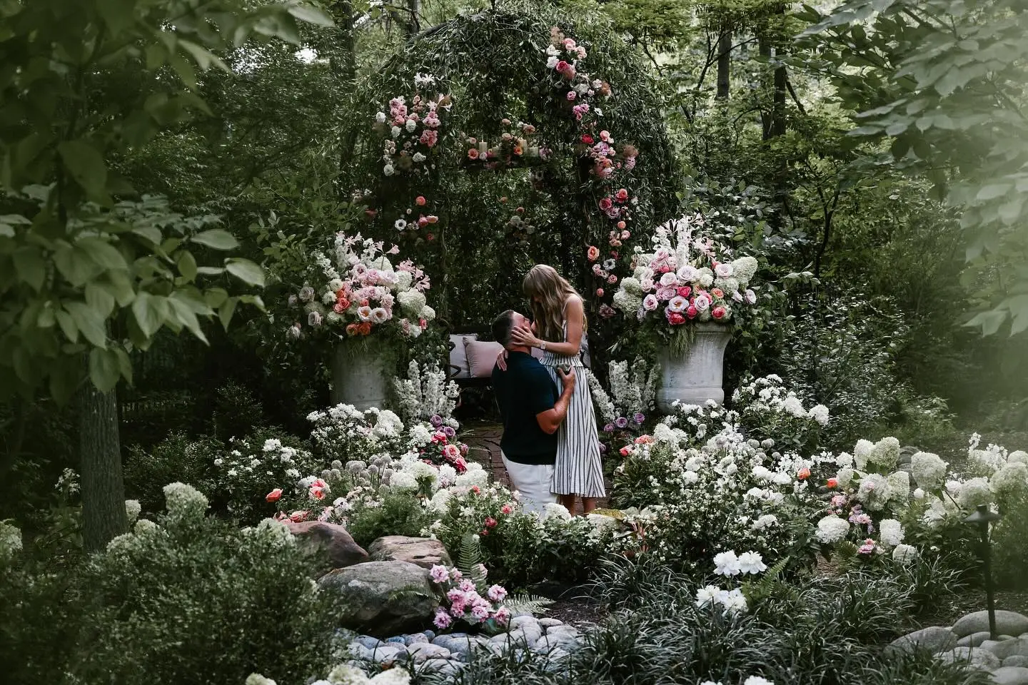 Taylor Swift and Travis Kelce embrace beneath a floral arch during their engagement.