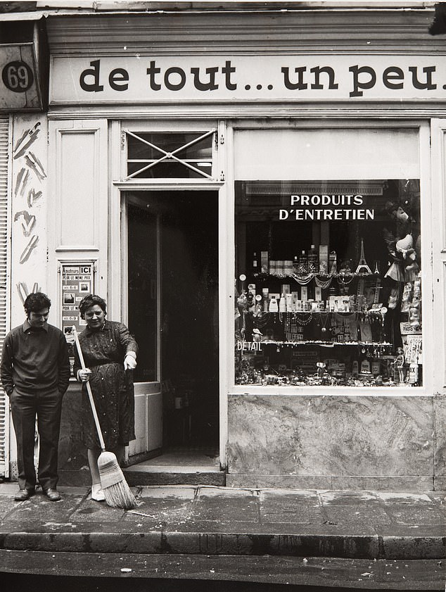 Shopkeeper sweeping the pavement outside a narrow storefront