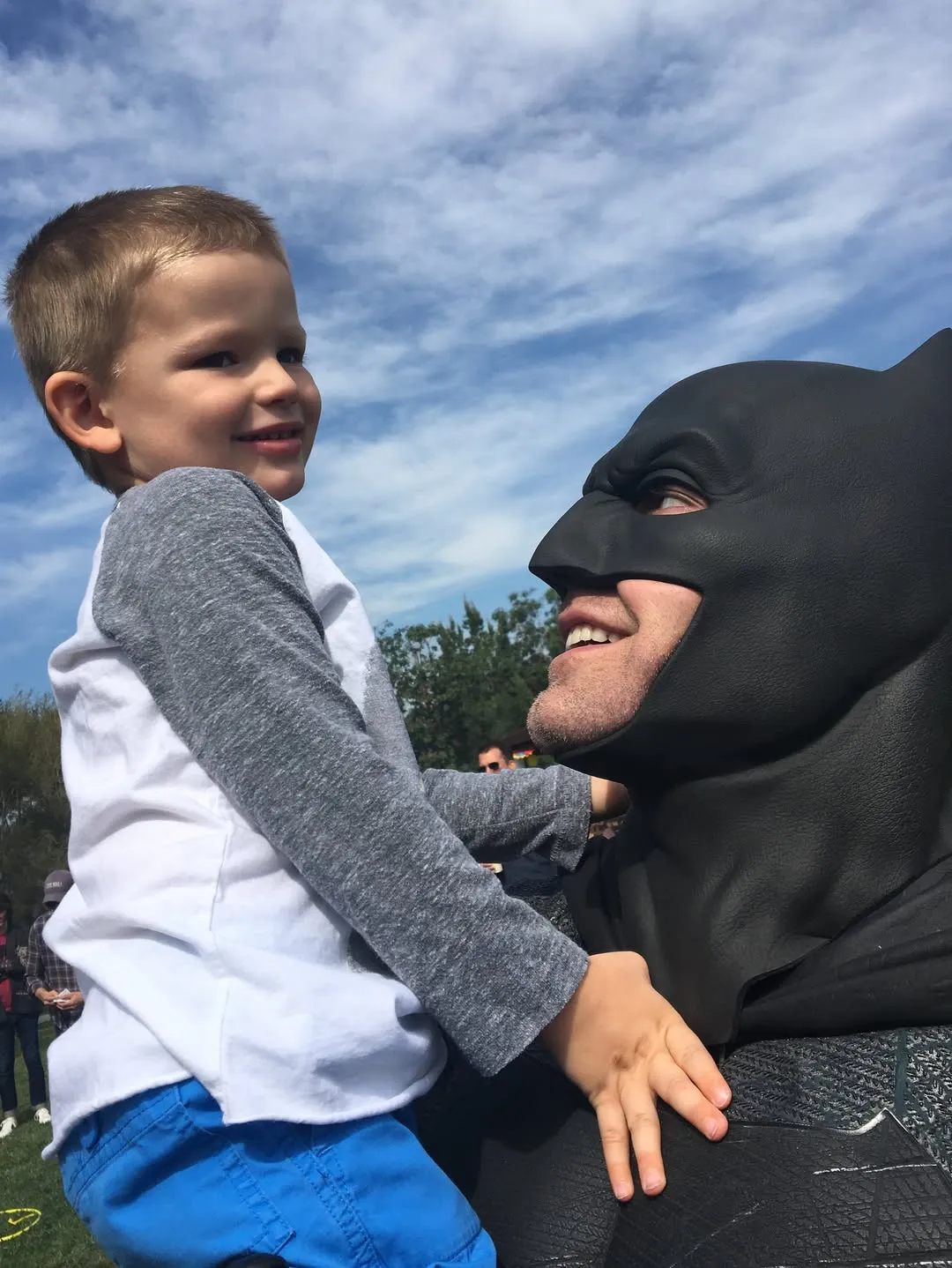 Ben Affleck in a Batman mask holding a child who is smiling.