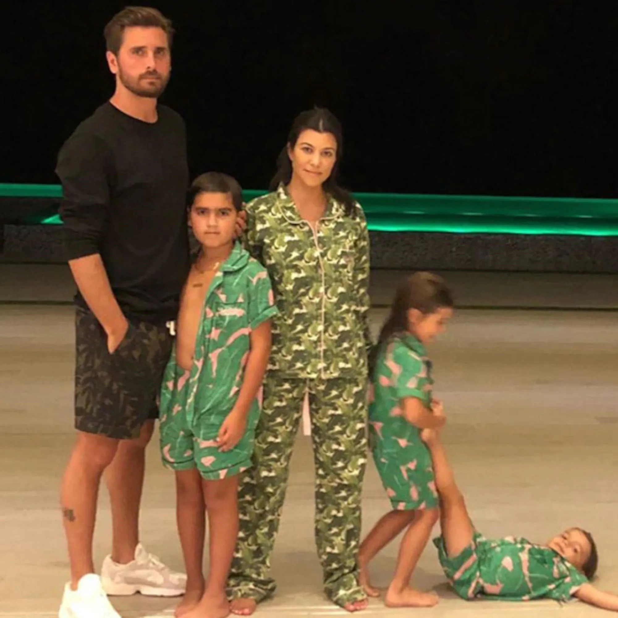 Scott Disick and Kourtney Kardashian with their three children, one of whom is lying on the floor while another stands over them holding their leg up.